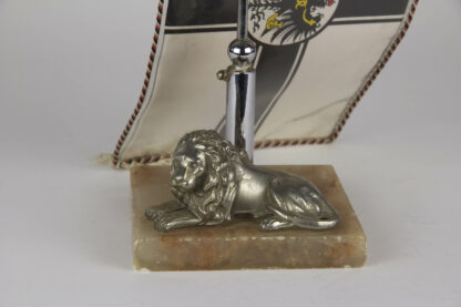 Tischfahnenständer, Anf. 20. Jh., auf Marmorsockel liegender Löwe, mit Ständer für eine Vereinsfahne, originell, Gebrauchsspuren. H: 66 cm.