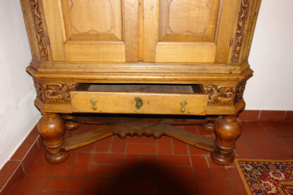 Stollenschrank, Barock, 2. Hälfte 18. Jh., norddeutsch, Eiche massiv, Korpus auf gedrechselten Säulen mit geschwungener Kreuzverstrebung, zweitürig, darunter zentrales Schubfach, Schubfach flankiert von zwei geschnitzten, geflügelten Löwen, neben den Türen säulenförmig floral geschnitzt, leicht gebogener Giebel, alt restauriert. H: 196 cm, B: 144 cm, T: 60 cm.