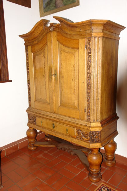 Stollenschrank, Barock, 2. Hälfte 18. Jh., norddeutsch, Eiche massiv, Korpus auf gedrechselten Säulen mit geschwungener Kreuzverstrebung, zweitürig, darunter zentrales Schubfach, Schubfach flankiert von zwei geschnitzten, geflügelten Löwen, neben den Türen säulenförmig floral geschnitzt, leicht gebogener Giebel, alt restauriert. H: 196 cm, B: 144 cm, T: 60 cm.