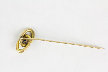 Krawattennadel, Anf. 20. Jh., gemarkt, 585er Gelbgold, zwei verschlungene Ringe, in der Mitte im Cabochon-Schliff gefasster Saphir, Gebrauchsspuren. L: 6,4 cm, 2,0 g.