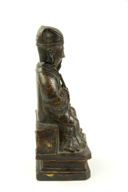 Figur, China, Ming Dynastie, 18. Jh., Eisen, überzogen mit Rotlack, teilweise mit Gold bemalt, Wenchang Wang, Daoistischer Gott der Kunst und Literatur, sitzend, mit Robe, Kopfbedeckung und Hu-Stab in den Händen, gefaltete Hände, auf Sockel, Reste von Goldlack, feine Patina, rückseitig Fünfzeichen-Marke, Gebrauchsspuren. H: 26 cm.