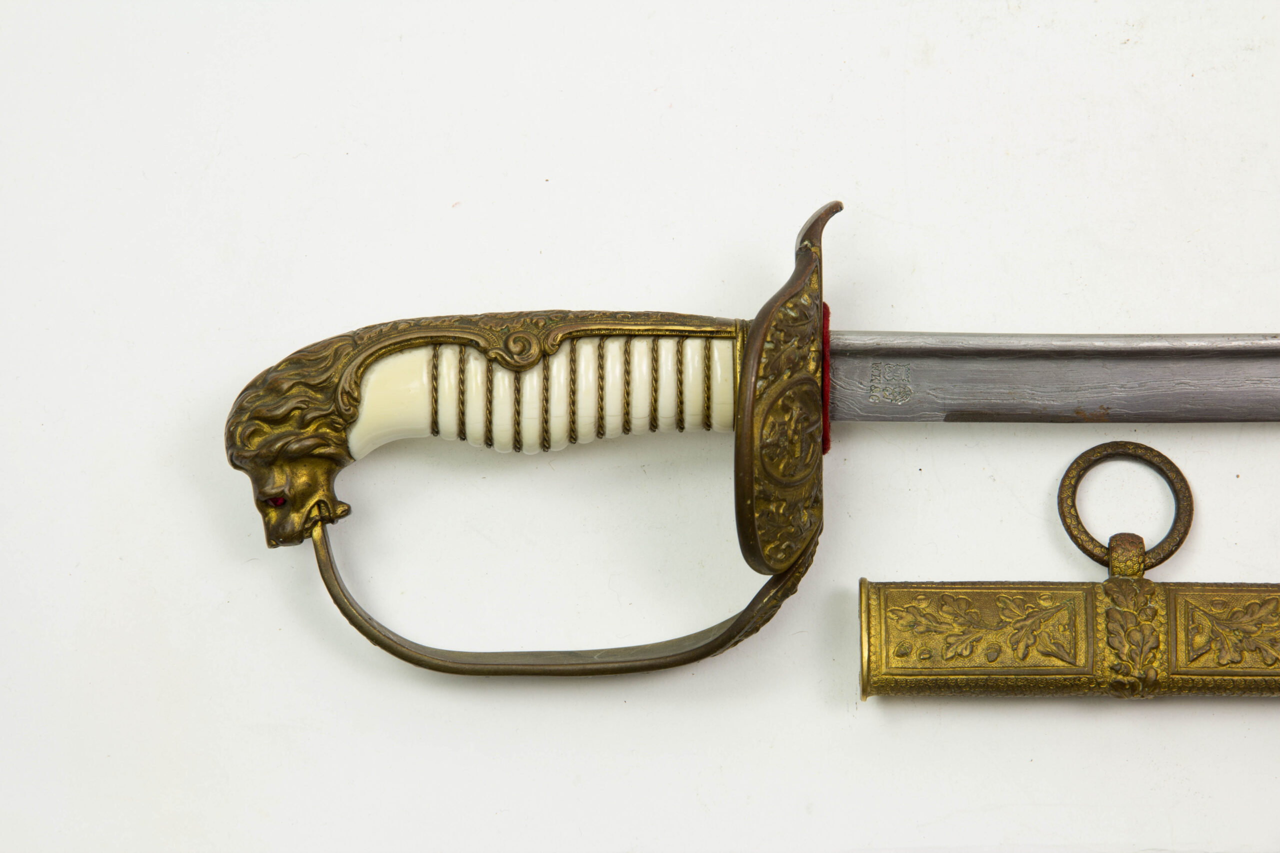 Marine-Säbel, Deutschland, Anf. 20. Jh., vergoldetes Bügelgefäß mit Löwenkopfabschluss, Augen aus zwei Glassteinen in rot (Backbord) und grün (Steuerbord), ausgesuchter Elfeneingriff mit Drahtwicklung, Gefäß mit zwei Klappscharnieren und Eichenlaubverzierungen mit Kaiserkrone, am inneren Scharnier Besitzerbezeichnung "Koch?", Stechrückenklinge von WKC in Streifendamast, Lederscheide mit drei vergoldeten und mit Eichenlaub verzierten Beschlägen, plastisch ausgearbeitete Tragbänder in Form von Eichenlaub, Trageringe verziert, unberührtes Stück mit Patina, hierbei kann es sich um ein Ehrenstück oder eine Luxuswaffe handeln, es gibt äußerst wenig bekannte Stücke dieser Ausführung, Gebrauchsspuren. L: 94 cm.