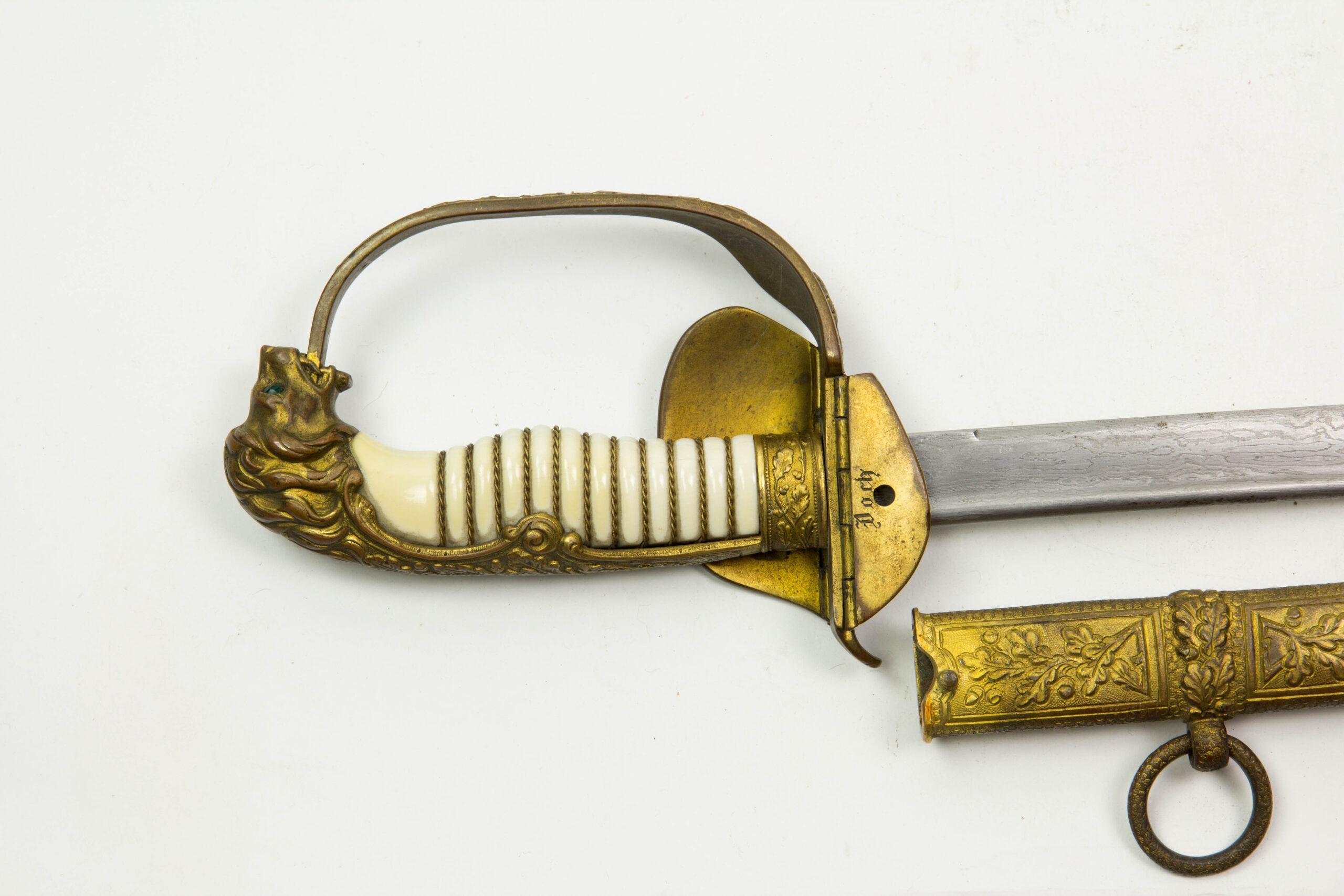 Marine-Säbel, Deutschland, Anf. 20. Jh., vergoldetes Bügelgefäß mit Löwenkopfabschluss, Augen aus zwei Glassteinen in rot (Backbord) und grün (Steuerbord), ausgesuchter Elfeneingriff mit Drahtwicklung, Gefäß mit zwei Klappscharnieren und Eichenlaubverzierungen mit Kaiserkrone, am inneren Scharnier Besitzerbezeichnung "Koch?", Stechrückenklinge von WKC in Streifendamast, Lederscheide mit drei vergoldeten und mit Eichenlaub verzierten Beschlägen, plastisch ausgearbeitete Tragbänder in Form von Eichenlaub, Trageringe verziert, unberührtes Stück mit Patina, hierbei kann es sich um ein Ehrenstück oder eine Luxuswaffe handeln, es gibt äußerst wenig bekannte Stücke dieser Ausführung, Gebrauchsspuren. L: 94 cm.