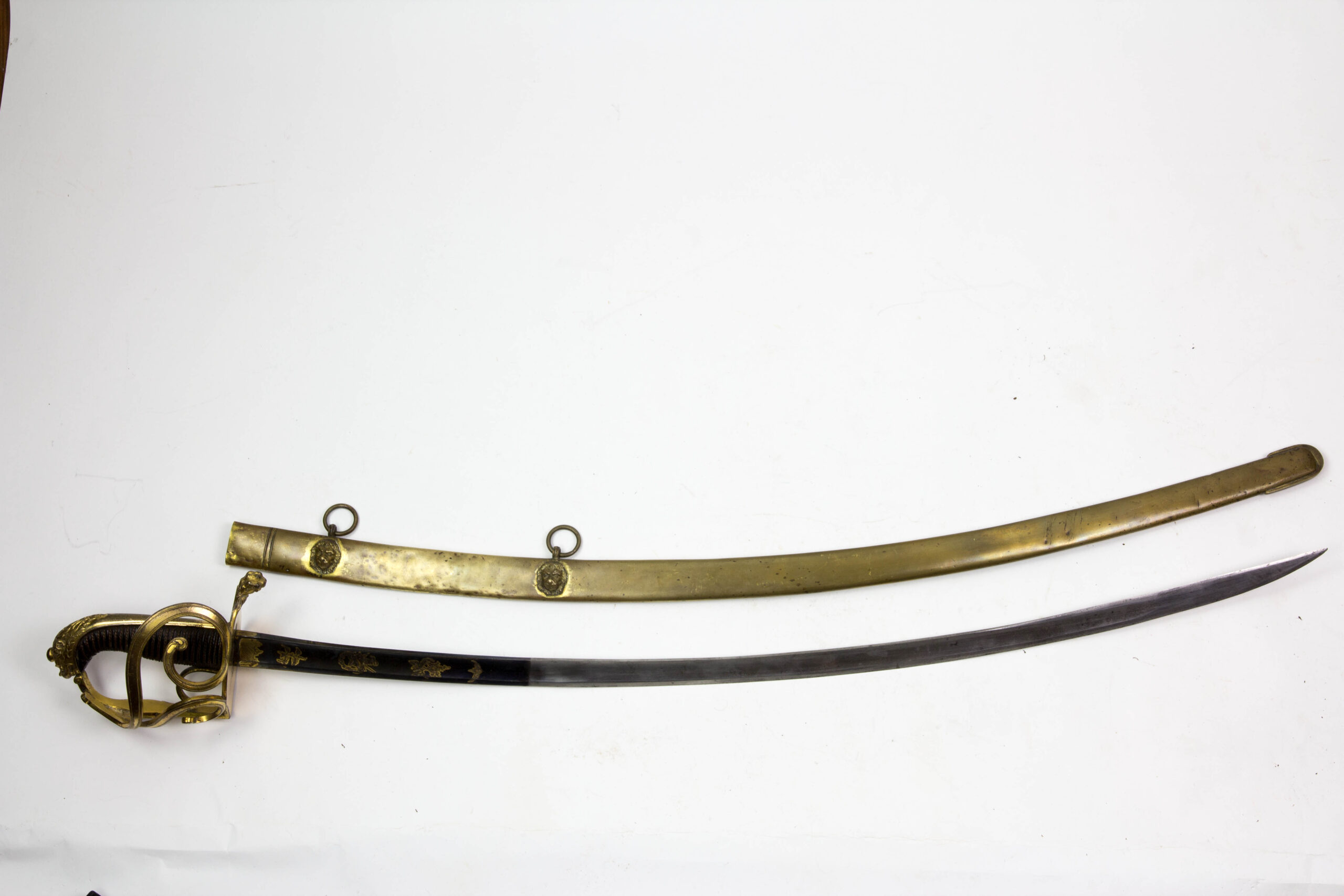 Offizierssäbel, Sachsen, nach 1806, Leibkürassier - Garde, Löwenkopfgefäß mit 3 Nebenbügeln, zwei davon eingerollt, Bronze, ovales Stichblatt in einer Löwentatze endend, Holzgriffstück mit Leber überzogen und Drahtwicklung, sächsisches Wappen auf dem Hauptbügel, Rückenklinge mit Hohlschliff, im ersten Drittel gebläut, vergoldet und mit Ornamenten und Kriegsgirlanden verziert, dazu Messingscheide mit zwei plastischen Löwenköpfen und Trageringen, Reste einer Vergoldung, absolut unberührtes Stück mit schöner Patina und guter Erhaltung, das Regiment wurde 1822 in Russland komplett aufgerieben, einzigartiges Stück. L: 101 cm.