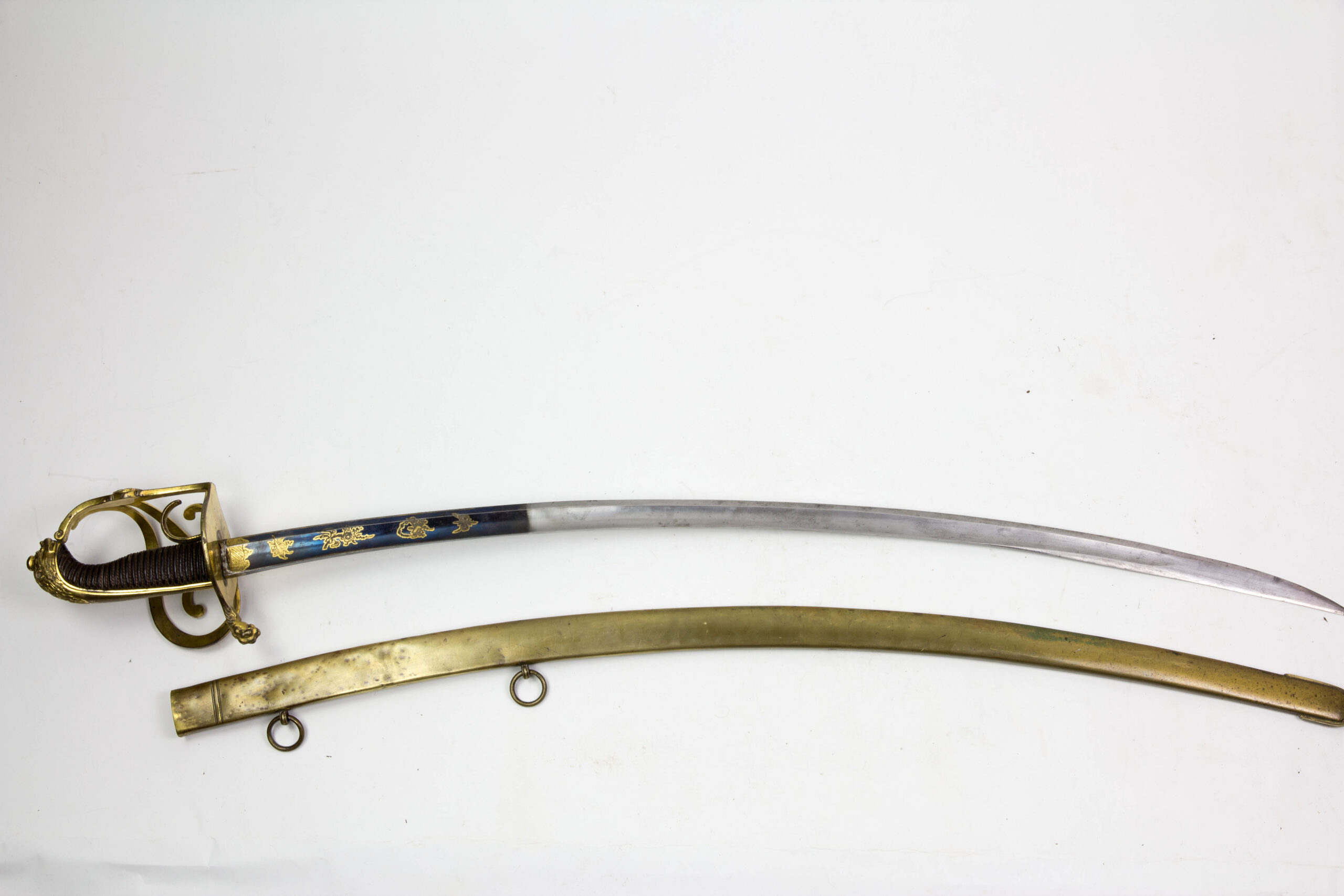 Offizierssäbel, Sachsen, nach 1806, Leibkürassier - Garde, Löwenkopfgefäß mit 3 Nebenbügeln, zwei davon eingerollt, Bronze, ovales Stichblatt in einer Löwentatze endend, Holzgriffstück mit Leber überzogen und Drahtwicklung, sächsisches Wappen auf dem Hauptbügel, Rückenklinge mit Hohlschliff, im ersten Drittel gebläut, vergoldet und mit Ornamenten und Kriegsgirlanden verziert, dazu Messingscheide mit zwei plastischen Löwenköpfen und Trageringen, Reste einer Vergoldung, absolut unberührtes Stück mit schöner Patina und guter Erhaltung, das Regiment wurde 1822 in Russland komplett aufgerieben, einzigartiges Stück. L: 101 cm.